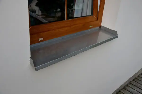Szary parapet zewnętrzny plastikowy pod drewnianym oknem.