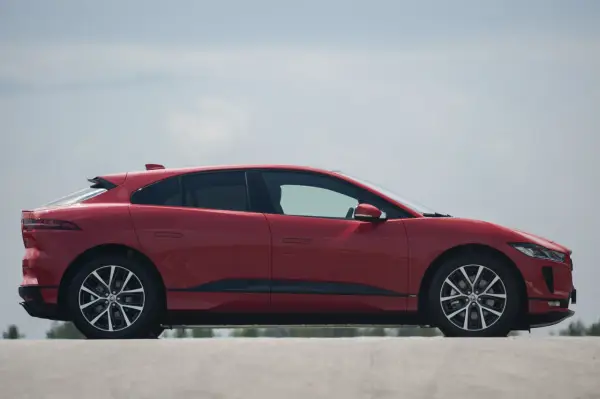 Czerwony jaguar elektryczny z profilu, z widocznymi felgami i linią dachu.