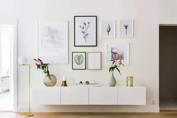 Ett modernt, vitt sideboard med konstverk ovanför, inklusive en Stockholmskarta och en flamingo. En golvlampa och vaser ger en stilfull touch.