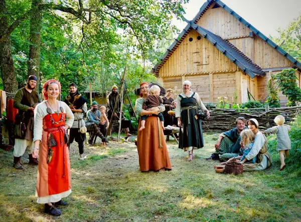 En grupp människor i vikingakläder samlas framför ett trädhus i vikingabyn Storholmen.