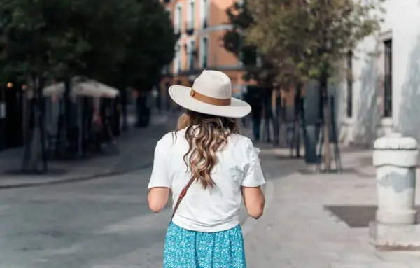 Une femme porte un chapeau et une robe fleurie, idéale pour savoir quelle couleur porter quand il fait chaud.