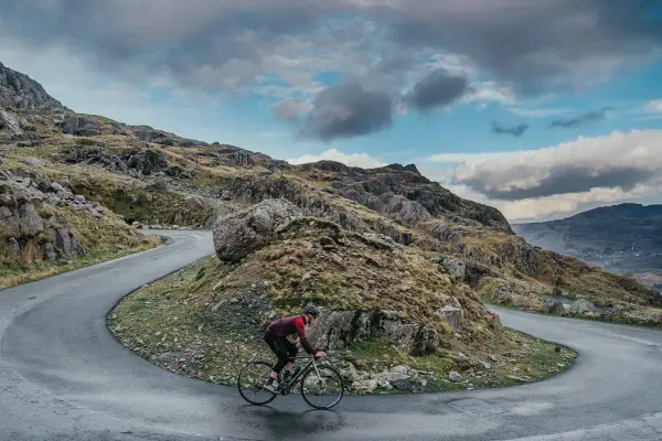 Ciclista en una carretera sinuosa en un paisaje montañoso, disfrutando de su aventura de España en bicicleta.
