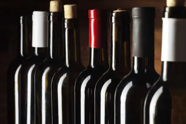 Une rangée de bouteilles de vin sombres, certaines avec des bouchons en liège, d'autres avec des capsules colorées. Un millésime Beaujolais pourrait se cacher parmi elles.
