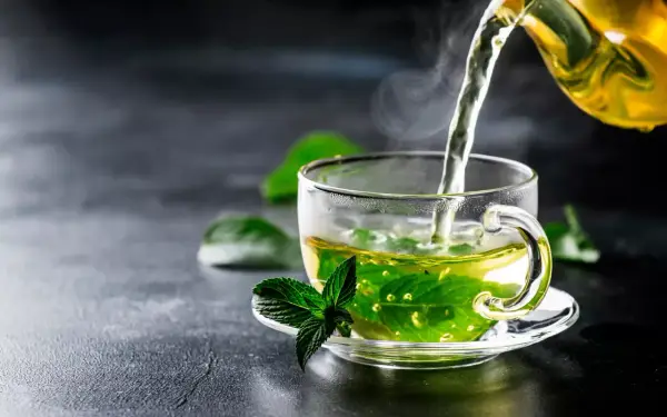 Un thé fumant à la menthe poivrée est versé dans une tasse transparente, ornée d'une feuille de menthe fraîche.