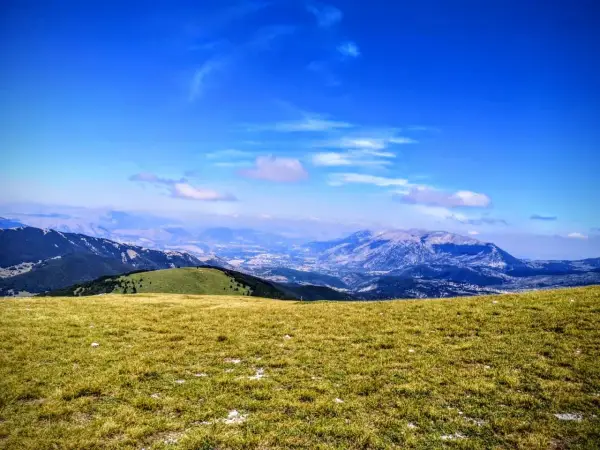 Prato verdeggiante con vista panoramica sul monte Pizzalto e le montagne circostanti sotto un cielo azzurro con nuvole sparse.