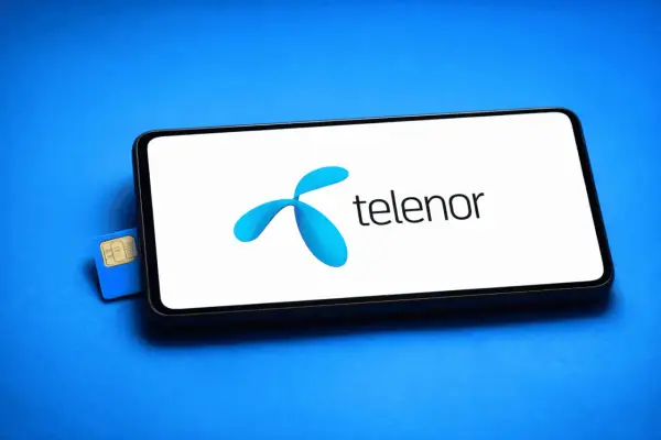 En blå Telenor simkort ligger bredvid en smartphone med Telenors logotyp på skärmen.