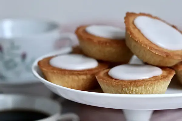 Små, gyllene mazariner med vit glasyr på ett tårtfat. Perfekt till fikat, här är ett enkelt mazariner recept.