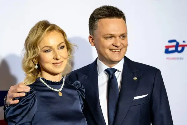 Szymon Hołownia z żoną, uśmiechnięci, pozują do zdjęcia. Ona w granatowej sukience i perłach, on w garniturze.