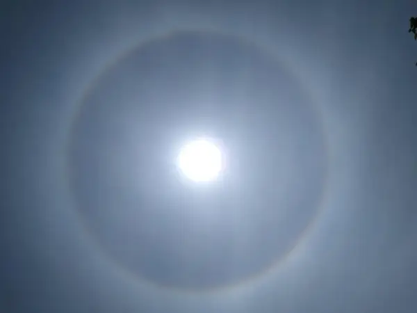 Jasne niebo z widocznym słońcem otoczonym tęczowym kręgiem. To piękny efekt halo.