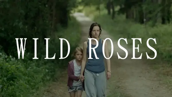 Kobieta i dziewczynka idą ścieżką w lesie. Napis "WILD ROSES" sugeruje, że to kadr z filmu.