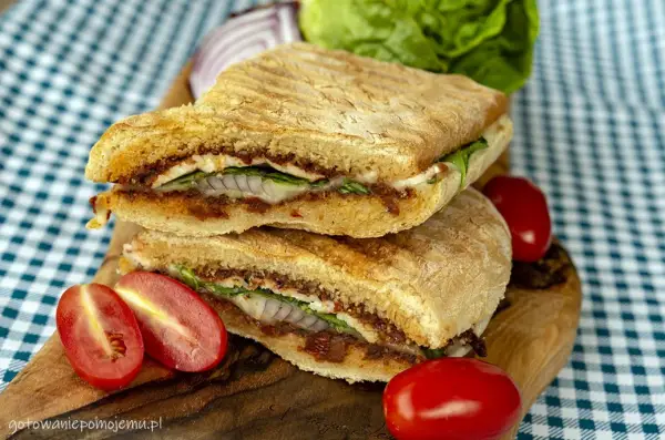 Pyszne panini z kurczakiem, suszonymi pomidorami i serem, podane z pomidorkami koktajlowymi i sałatą.