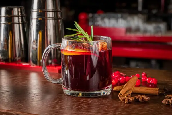 Aromatyczny grog z pomarańczą i rozmarynem, ozdobiony laskami cynamonu i gwiazdkami anyżu, kusi na drewnianym blacie.