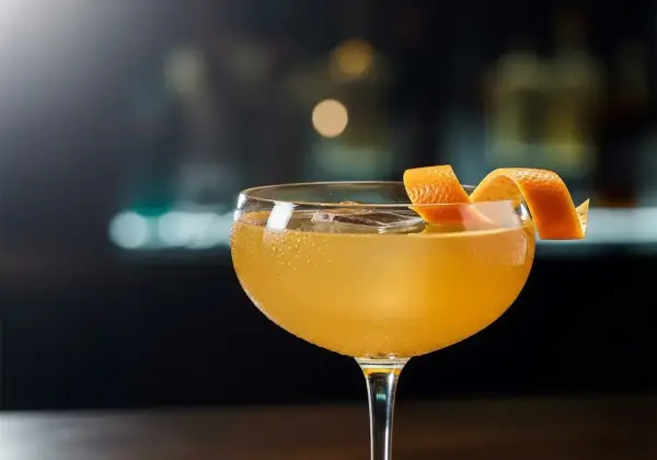 En gyllene cocktail i ett coupeglas, garnerad med en apelsinzest. Ett klassiskt, old fashioned recept som lockar.