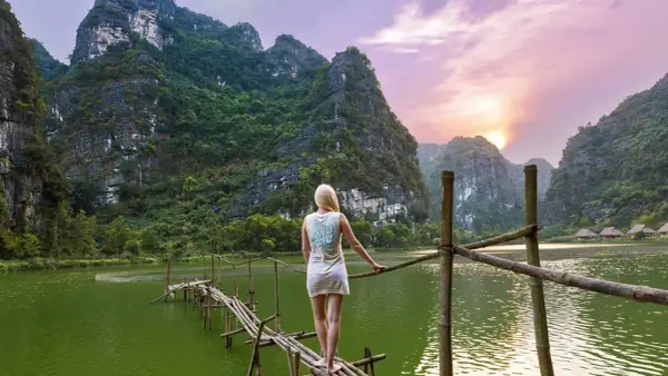 Frau auf Bambusbrücke in Vietnam, umgeben von Karstbergen und einem See. Tolle Reise-Hacks für unvergessliche Momente.