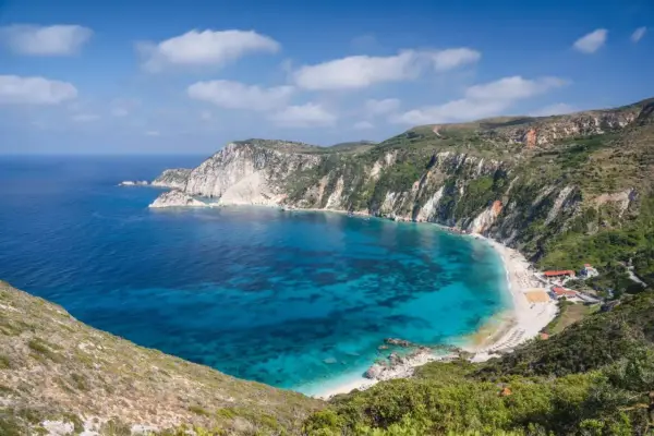 Malownicza zatoka z turkusową wodą i piaszczystą plażą, otoczona stromymi, zielonymi klifami. To idealne miejsce na wypoczynek na wyspie na Morzu Jońskim.