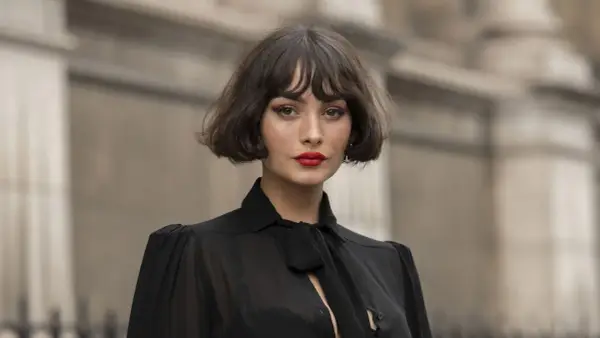 Mujer con un elegante corte de pelo **french bob**, labios rojos vibrantes y un top negro con lazada.