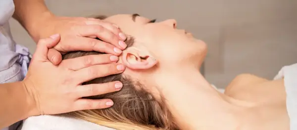 Mains douces appliquant une thérapie cranio sacrée sur la tête d'une femme détendue.