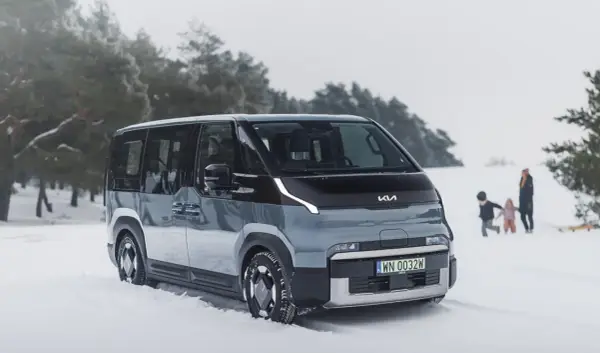 Szary elektryczny minivan Kia EV9 na śniegu, z rodziną w tle.