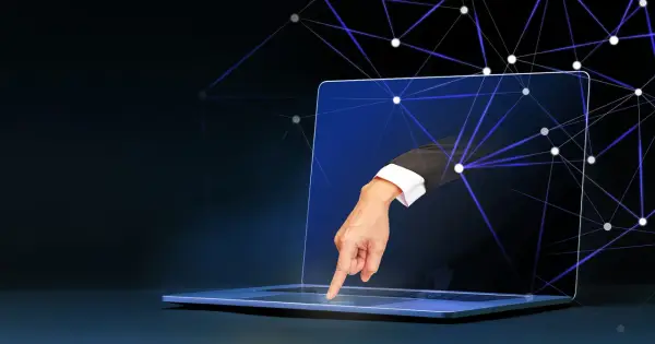 Ręka w garniturze wychodzi z ekranu laptopa, dotykając klawiatury. Sieć połączeń symbolizuje zdalny dostęp do komputera.