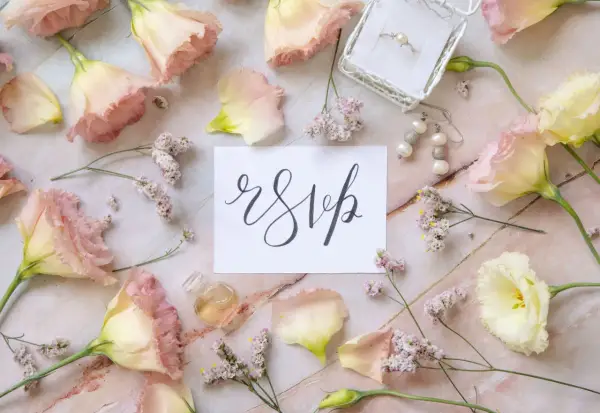 Delikatne kwiaty i biżuteria otaczają kartkę z napisem "rsvp".