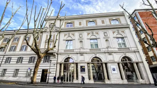 Le **Palazzo Merulana**, un édifice élégant, se dresse sous un ciel bleu nuageux, orné d'arbres dénudés aux branches graphiques.