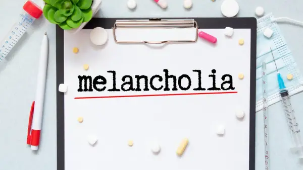Na kartce widnieje napis "melancholia". Wokół leżą tabletki, strzykawka i maseczka, sugerując walkę z tym stanem.