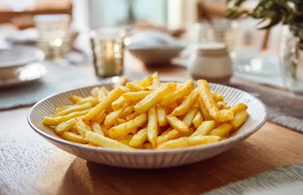 Un plato lleno de patatas fritas doradas y crujientes, listo para ser disfrutado en una mesa bien puesta.