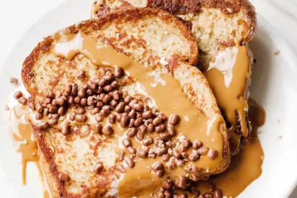 Tostadas francesas cubiertas con crema de cacahuete y crujientes bolitas de chocolate. Un desayuno delicioso y tentador.