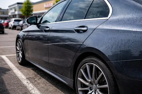 Ciemny samochód na parkingu z widocznym, długim, nieświadomym zarysowaniem na drzwiach.