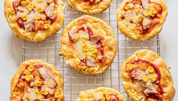 Mini pizze z serka wiejskiego, z kukurydzą i kawałkami mięsa, ułożone na metalowej kratce.