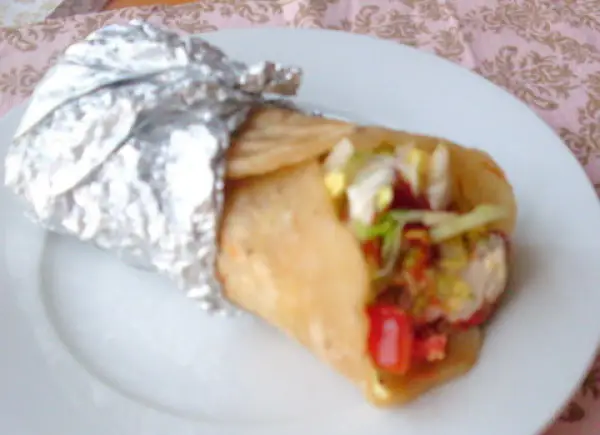 Pyszny placek z kebabem, zawinięty w folię aluminiową, z widocznym nadzieniem z warzyw i mięsa.