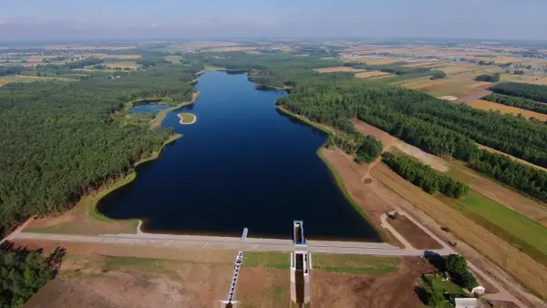 Widok z lotu ptaka na zalew Jagodno otoczony lasem i polami. Na pierwszym planie zapora z budowlami technicznymi.