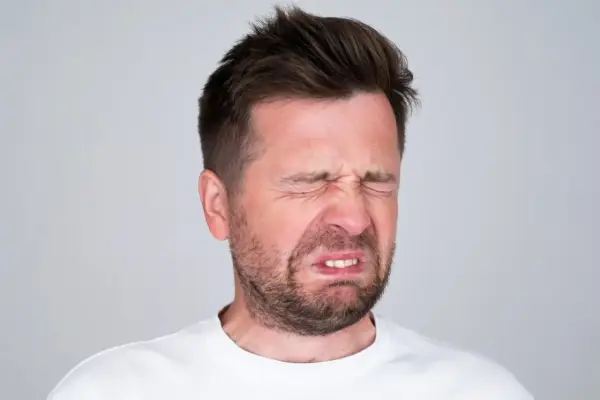 Mężczyzna z wykrzywioną twarzą, oczy zamknięte, czuje gorzki smak w ustach.