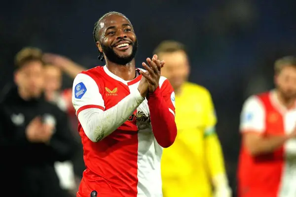 Uśmiechnięty Raheem Sterling w czerwono-białej koszulce, klaszczący. Jego statystyki w tym sezonie są imponujące.