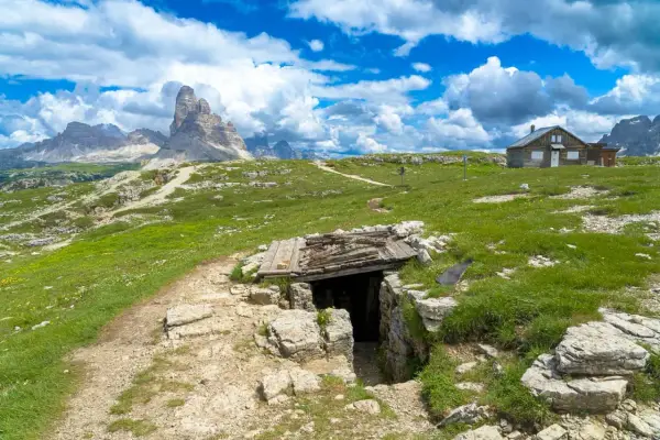 Un sentiero conduce a un rifugio di guerra sul Monte Piana, con le maestose Tre Cime di Lavaredo sullo sfondo.