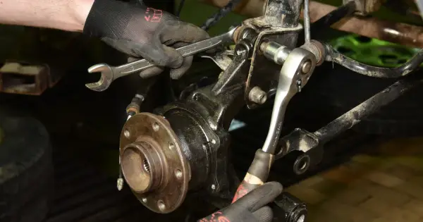Mechanik dokręca śruby przy piaście, wymieniając łożysko w samochodzie.