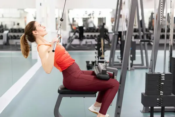 Kvinna tränar rakarmade latsdrag på gym.