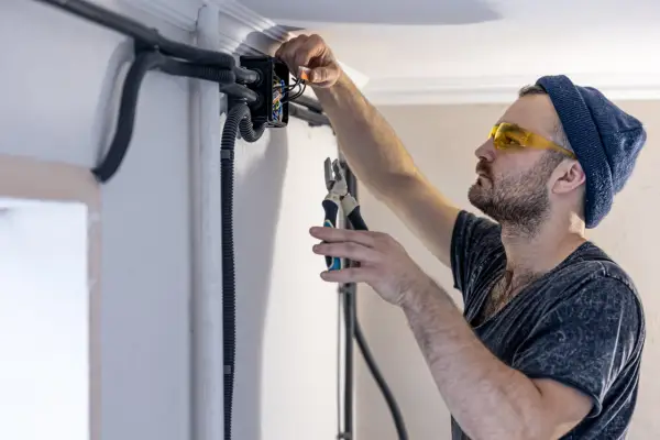 Elektryk w okularach ochronnych montuje przewody bezhalogenowe w puszce instalacyjnej, używając szczypiec.