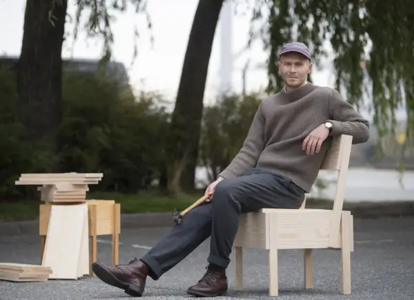 Erik Eje Almqvist sitter på en trästol med en hammare i handen, omgiven av trämaterial.