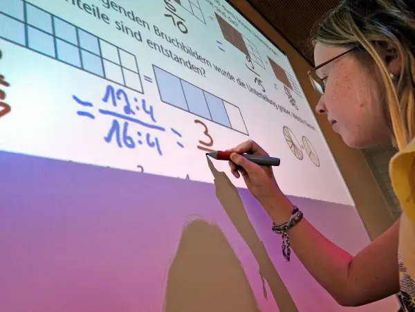 Ein Mädchen schreibt auf einem interaktiven Whiteboard, das Matheaufgaben zeigt. Solche Whiteboards sind moderne Tafeln für den Unterricht.