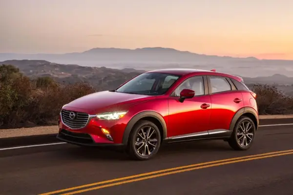 Czerwona Mazda CX-3 na tle górskiego krajobrazu o zachodzie słońca. Elegancka linia nadwozia i lśniący lakier.