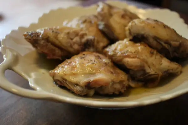 Plusieurs hauts de cuisse de poulet rôtis, assaisonnés d'herbes, reposent sur une assiette en céramique crème.