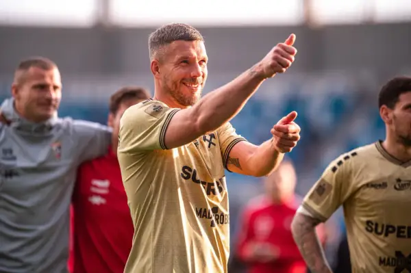 Uśmiechnięty Lukas Podolski pokazuje kciuk w górę, jakby podsumowywał swoje świetne statystyki.