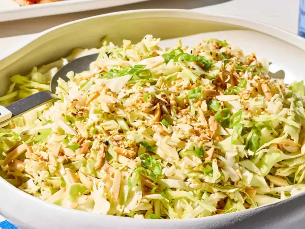 A refreshing Japanese cabbage recipe salad, topped with toasted almonds, sesame seeds, and green onions, served in a white bowl.