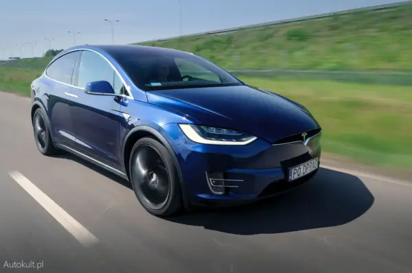 Granatowy Tesla Model X w ruchu na drodze, z widocznym kierowcą.