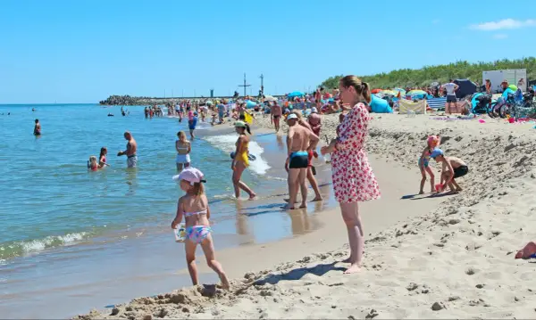 Słoneczne wczasy pod gruszą na plaży. Ludzie kąpią się w morzu i opalają na piasku. Dzieci bawią się w wodzie i budują zamki z piasku.