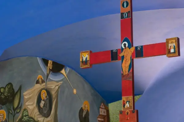 Czerwony krzyż z ikonami i malowidła ścienne przedstawiające sceny religijne, tworzące atmosferę sakralną.