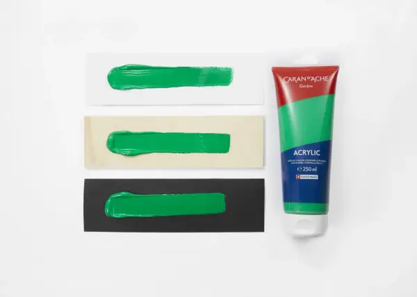 Bandeaux de peinture verte sur papier blanc, bois et noir, à côté d'un tube de gouache Caran d'Ache.