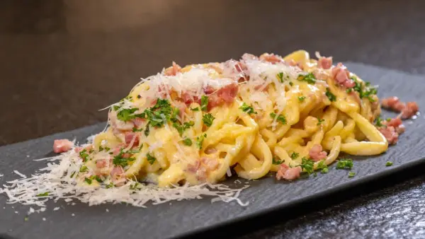 Eine Portion echte Carbonara mit cremiger Sauce, Guanciale und frisch geriebenem Parmesan auf einem dunklen Teller.
