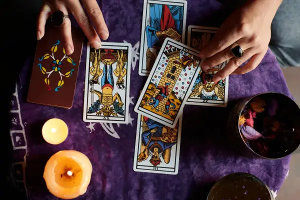 Manos de tarotista que es, barajando cartas y velas encendidas sobre tela morada.